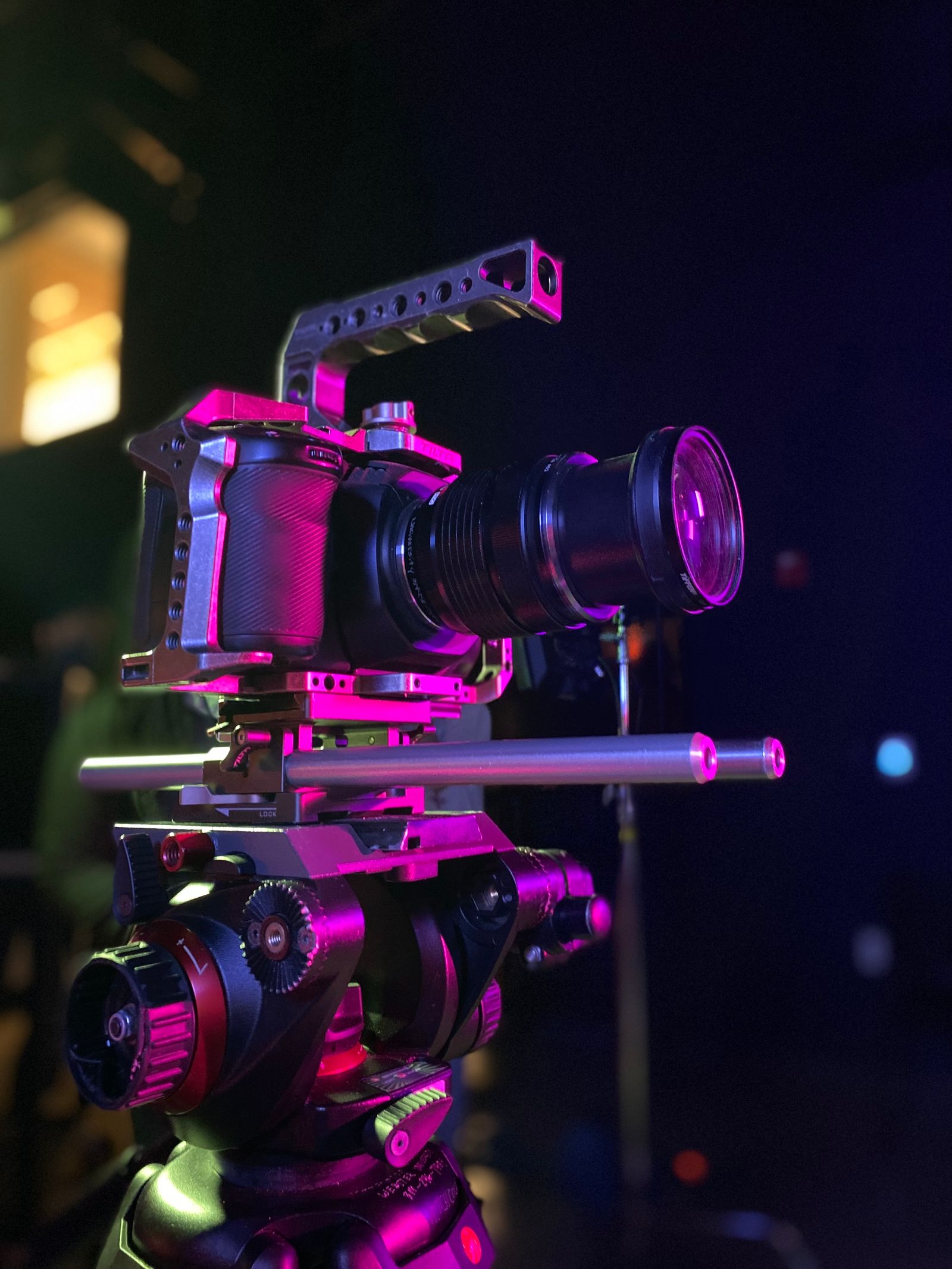 A cinema camera on a rig under pink light.